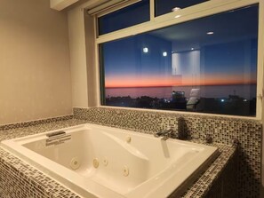 Una bañera grande con vista a un atardecer a través de una ventana.