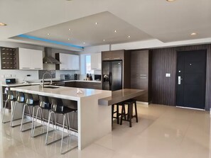 A modern kitchen with a central island, bar stools, and a dining table. - Sky Penthouse with Panoramic Ocean View & Jacuzzi (Tijuana)
