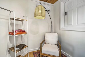 Une pièce avec une chaise blanche, une étagère blanche contenant des jeux de société, une lampe en osier et une porte blanche.