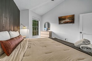 Ein Schlafzimmer mit einem Bett, einer Kommode, einem Spiegel, einem Fenster und einem Bild an der Wand.