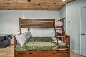 A bunk bed with a wooden frame and green bedding, a small bedside table with a bottle, and a wall-mounted thermostat. - Mountain Vista: Modern Cabin with Mt. LeConte View & Hot Tub (Gatlinburg)