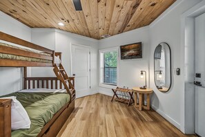 Une chambre avec un lit superposé, un bureau avec une chaise, un miroir et une fenêtre avec des stores.