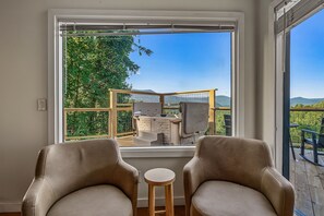 Ein Zimmer mit zwei Ledersesseln, einem kleinen Holztisch und einem großen Fenster mit Blick auf Grünflächen und Berge.