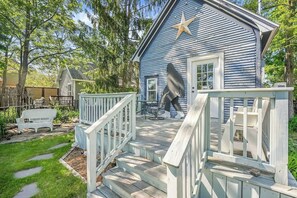 A blue house with a star on the roof, a porch with white railings, and a garden with a white bench. - Canvas & Coast DT TC, Games + Fire Pit | Pets Ok (Traverse City)