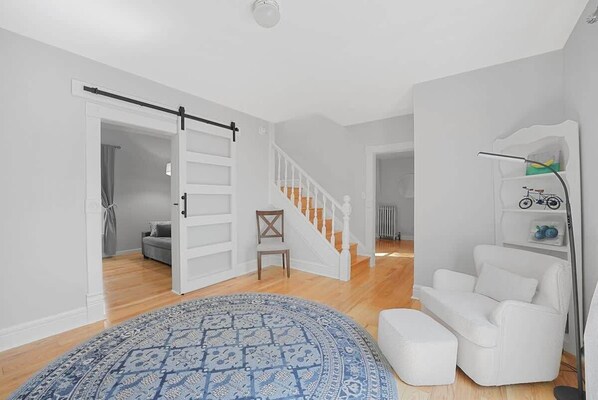 A spacious living room with a large rug, a white sofa, a chair, and a staircase. - Canvas & Coast DT TC, Games + Fire Pit | Pets Ok (Traverse City)