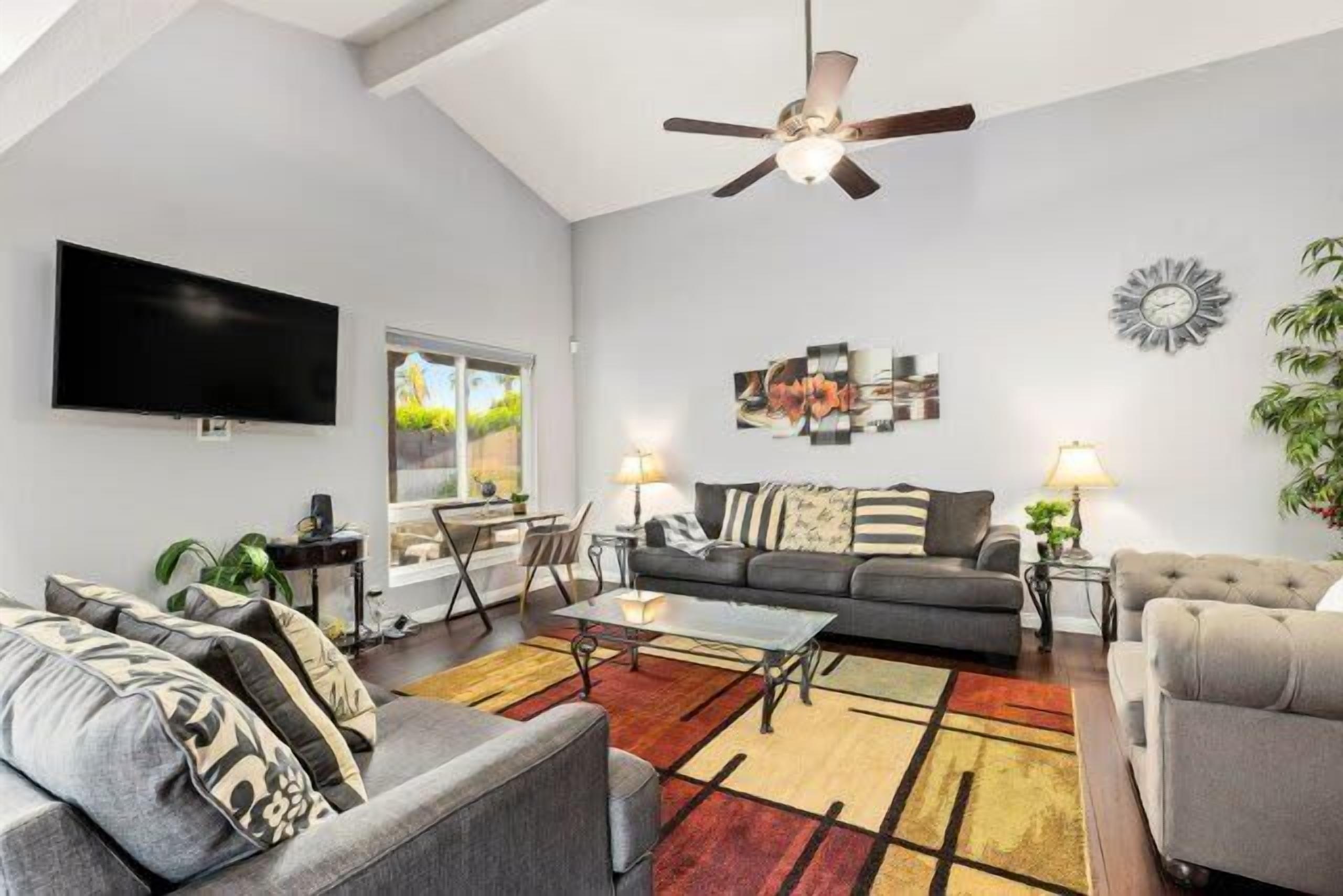 A living room with a ceiling fan, a flat-screen TV, a sofa, a coffee table, and a rug.
