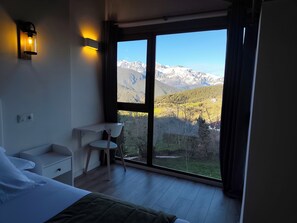 Ein Schlafzimmer mit Bett, Nachttisch, Stuhl und einem großen Fenster mit Bergblick.