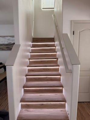 Eine Holztreppe mit weißen Geländern und einer weißen Tür am Obergeschoss.