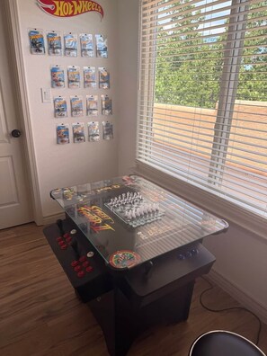 Une pièce avec une table dont le plateau est en verre, sur laquelle on trouve un jeu d’échecs et, accrochée au mur, une collection de voitures Hot Wheels.