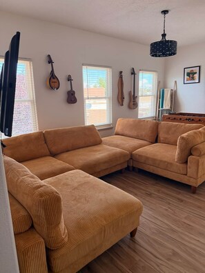 Un salon avec un canapé d’angle, un plancher en bois et des guitares accrochées au mur.
