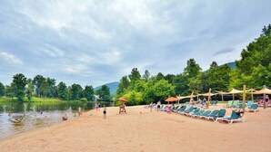 Una platja a la vora d'un llac amb gandules i ombrelles, una torre de socorristes i una massa d'aigua tranquil·la.