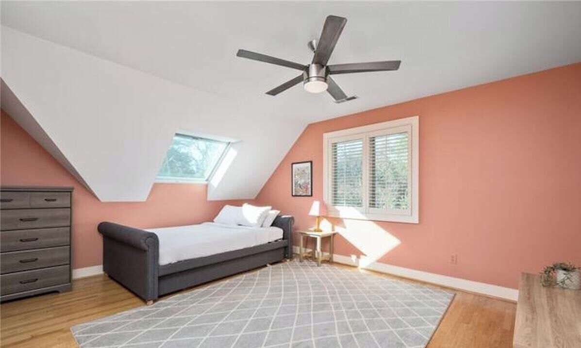 Une chambre à coucher avec un lit, une commode, un ventilateur de plafond, une fenêtre et une lampe.