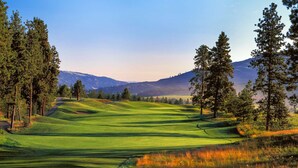 Ein Golfplatz mit sanften, grünen Hügeln, Bäumen und fernen Bergen.