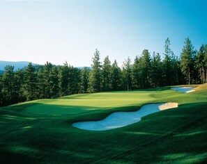 A golf course with a well-maintained green, sand bunkers, and a forested backdrop. - Pinnacle Pointe | 2 Bed Golf Getaway (Kelowna)
