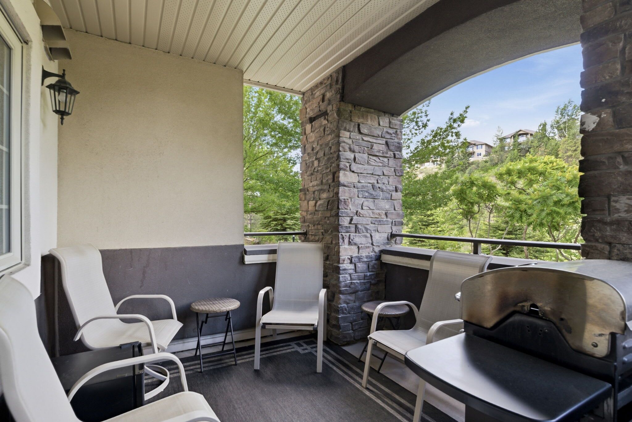 A balcony with seating, a stone pillar, and a view of greenery.
