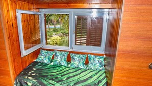 A wooden cabin room with a bed, a window, and a view of greenery outside.