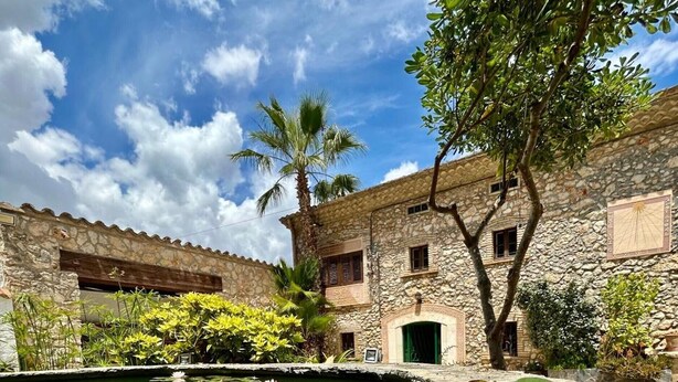 A stone building with a courtyard, a pond with water lilies, and a clear sky.