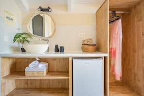Ein kleines Badezimmer mit rundem Spiegel, weißem Waschbecken, kleinem Kühlschrank, einer Pflanze und einem Holzschrank.