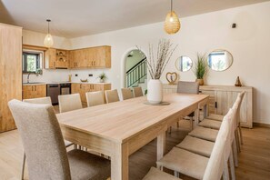 Eine moderne Küche mit Holzschränken, einem Esstisch mit Stühlen und Pendelleuchten.