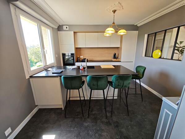 A modern kitchen with a central island, green bar stools, and a view of the outdoors.