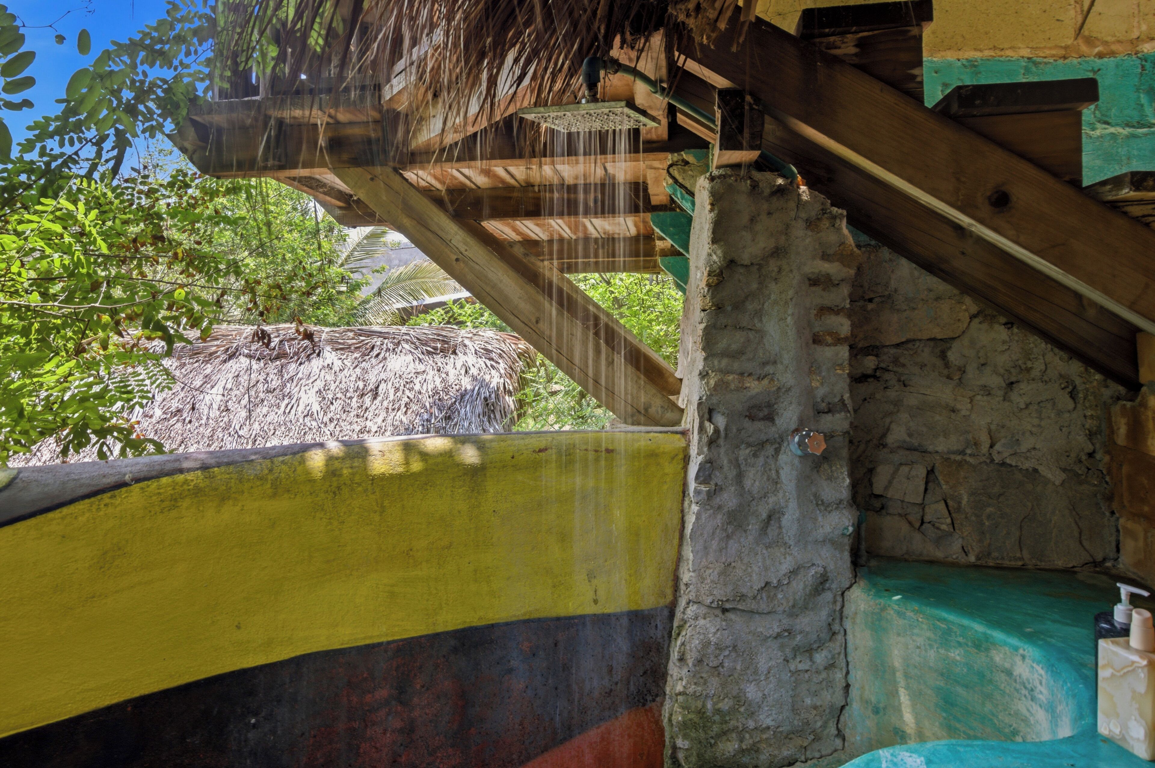 A rustic structure with a thatched roof, a wooden beam, and a partially visible yellow and black painted wall.