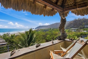A balcony with a view of the beach, a palm tree, and a thatched roof structure. - EL Copal (Mazunte)
