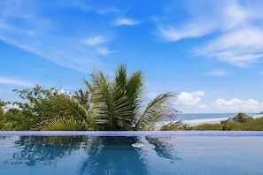 Cielo azul despejado, piscina y playa con palmeras.