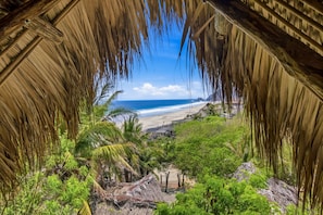 A thatched-roof structure with a view of a beach and lush greenery. - EL Copal (Mazunte)