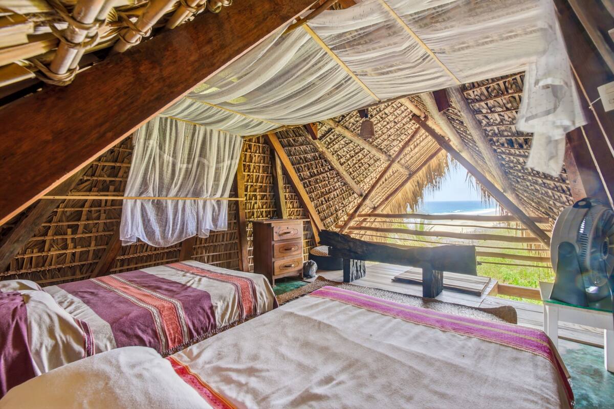 A room with a sloped ceiling, a bed, a wooden chest, and a fan.