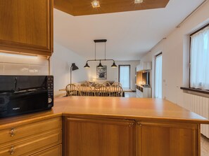A modern kitchen with wooden cabinets, a built-in microwave, and a dining area with a table and chairs. - Apartment Sun by Interhome (Pinzolo)
