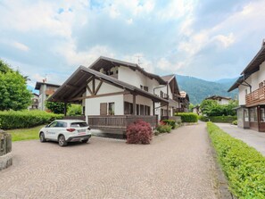 Ein traditionelles Chalet mit geneigtem Dach und Holzbalkonen, einer gepflasterten Auffahrt und einem geparkten Auto davor.