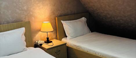 A hotel room with two beds, a bedside lamp, a wall-mounted air conditioner, and a wooden headboard.