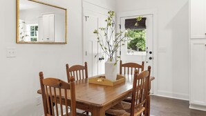 Et spiseområde med et træbord, fire stole, en vase med grene og et spejl på væggen.