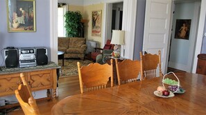 Un coin repas avec une table en bois, des chaises, un buffet garni de fruits, un canapé, un radiateur et une affiche accrochée au mur.