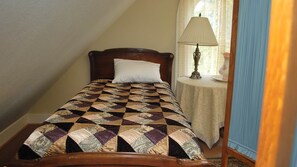 A single bed with a quilt, a bedside table with a lamp, and a window with curtains. - Experience Luxury Historic Home Near Beach and Astoria (Warrenton)