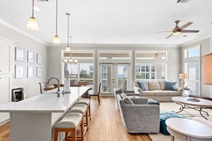 Eine geräumige Küche mit einer zentralen Kochinsel, ein Essbereich mit Tisch und Stühlen, eine Sitzecke mit Sofa sowie ein Deckenventilator.