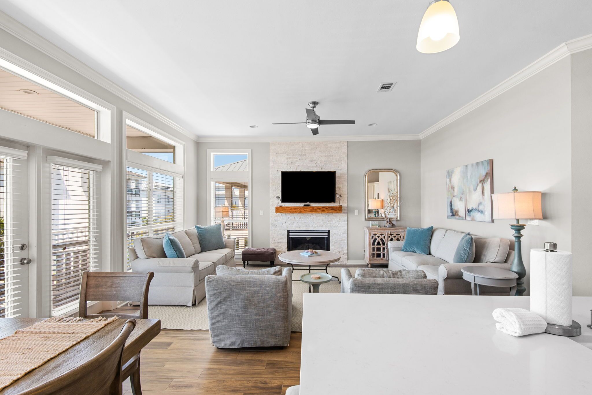 A spacious living room with a fireplace, a ceiling fan, and a large TV mounted above it.