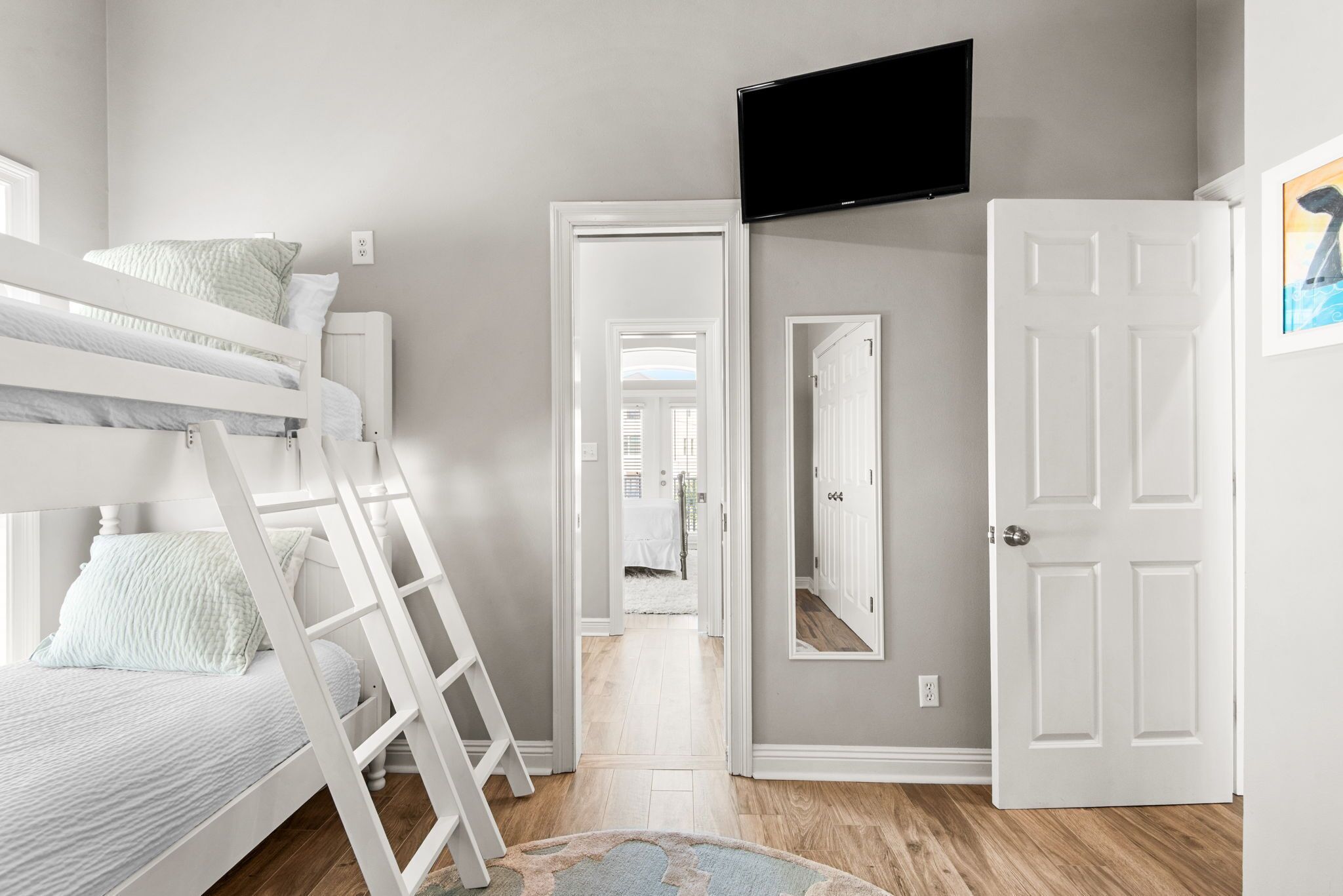 A bedroom with a bunk bed, a TV mounted on the wall, and a door leading to another room.