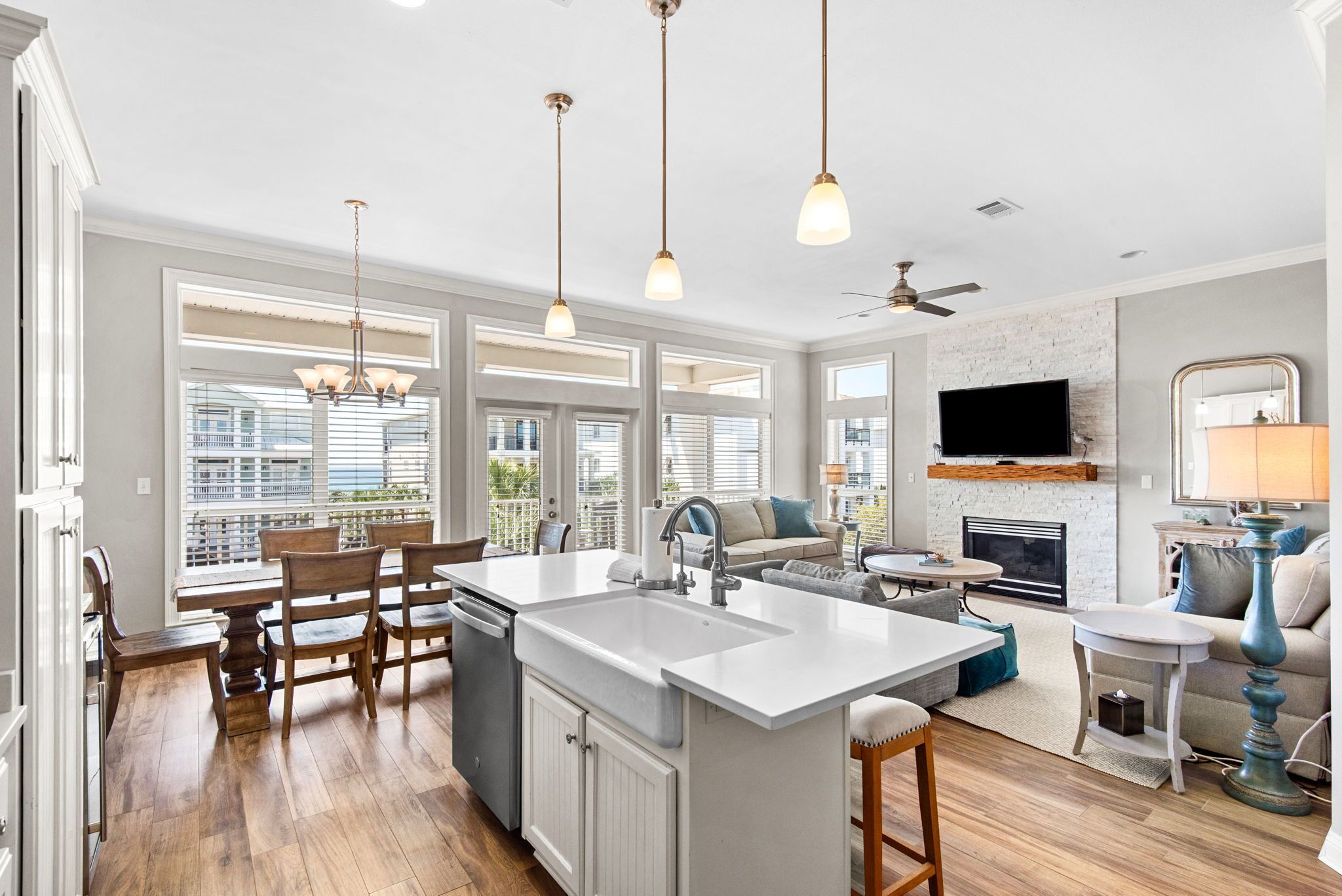 A modern kitchen with a central island, dining area with chairs, a sofa, a TV, and a fireplace.