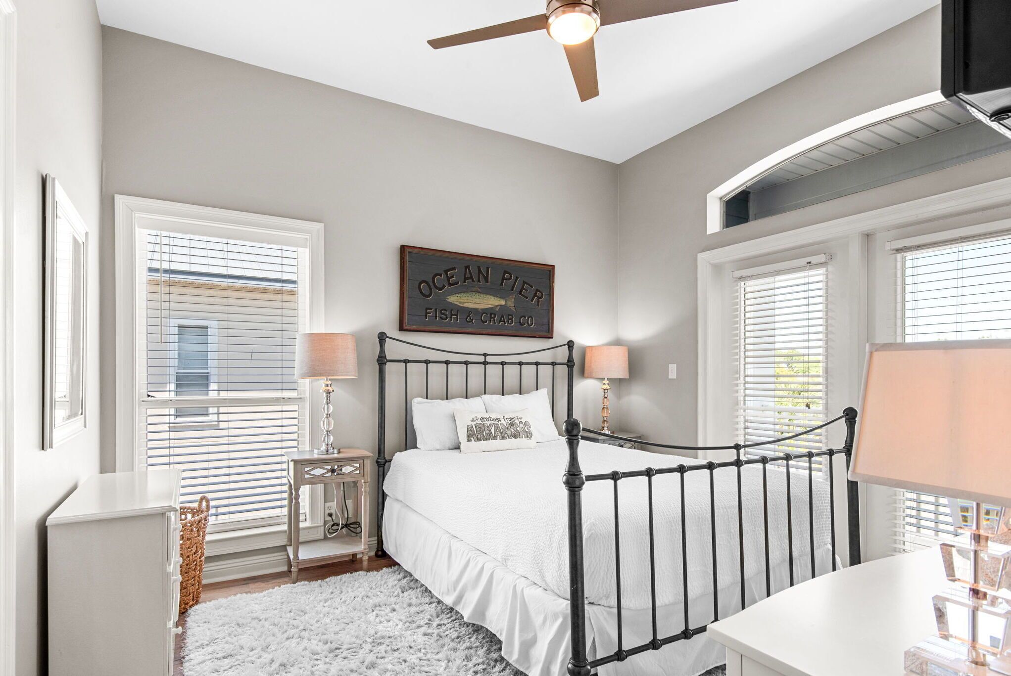 A bedroom with a bed, two bedside lamps, a ceiling fan, and a window with blinds.