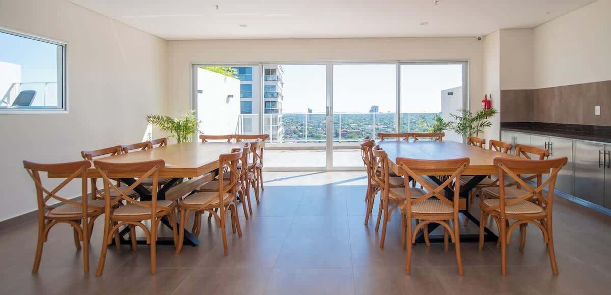 A spacious dining area with a large table and chairs, a kitchen area, and a balcony with a city view.