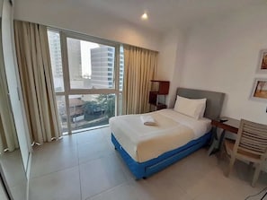 Habitación de hotel con cama, escritorio, silla, ventana con cortinas y vista a edificios.