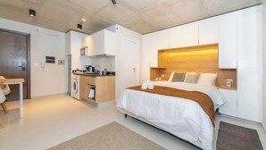 A modern hotel room with a large bed, a wooden headboard, a kitchenette, and a separate seating area. - Modern Studio with Pool, Gym & Balcony in Asunción (Asunción)