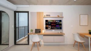 A modern living room with a glass door, a wooden desk with a laptop, two white chairs, and a wall-mounted shelf with various items. - Modern Studio with Pool, Gym & Balcony in Asunción (Asunción)