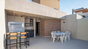 An outdoor patio with a grill, dining table, and chairs. - Modern Studio with Pool, Gym & Balcony in Asunción (Asunción)