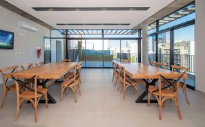 Una amplia sala de reuniones con una larga mesa de madera y sillas, ventanas grandes con vistas a la ciudad y un diseño de techo moderno.