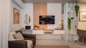 Uma sala de estar moderna com um sofá, uma mesa de centro, uma TV na parede e uma estante de livros.