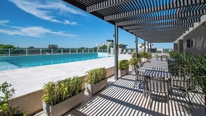 Et tagområde med swimmingpool, pergola, udendørs møbler og krukker med planter.