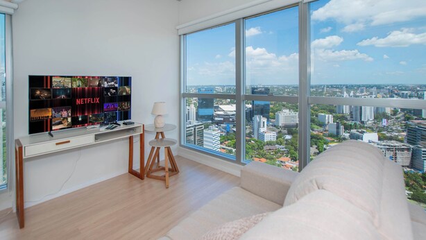 A modern room with a large TV displaying Netflix content, a desk, a lamp, and a large window offering a city view. - Urban High-floor One BR Escape, Petra Tower (Asunción)