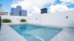 A rooftop swimming pool with a tiled edge, surrounded by white walls and some greenery. - Stylish One BR,King bed,Pool, Gym, BBQ, Prime Area (Asunción)